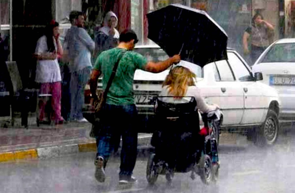 Man holding umbrella for wheelchair bound woman